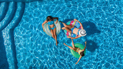 Family in swimming pool aerial drone view from above, happy mother and kids swim on inflatable ring donuts and have fun in water on family vacation, tropical holidays on resort