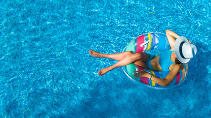 Beautiful girl in hat in swimming pool aerial top view from above, woman relaxes and swims on inflatable ring donut and has fun in water on family vacation, tropical holiday resort