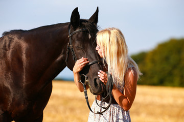 Horse with owner in portrait on a summer field, owner cuddles with her horse.