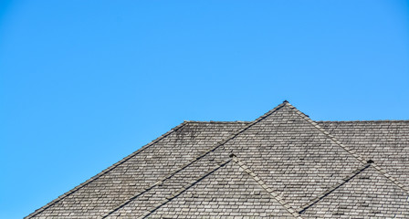 Fototapeta na wymiar Massive roofs of residential house on blue sky background. Family house with big roofs tiled by wooden shingles