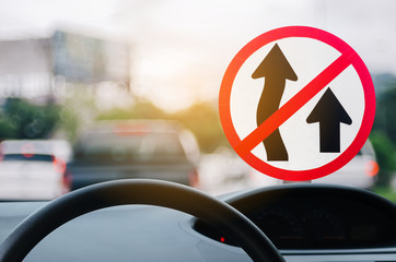 Fototapeta premium No Overtaking warning sign and inside car view ,steering wheel on blur traffic road with colorful bokeh light abstract background.