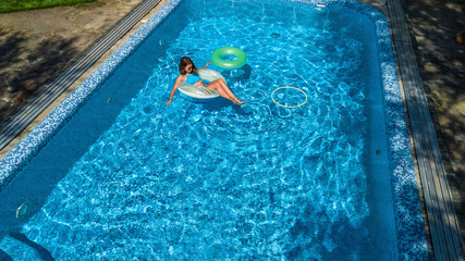 Aerial view of beautiful girl in swimming pool from above, swim on inflatable ring donut and has fun in water on family vacation on tropical holiday resort
