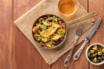 Rustic mushrooms and olives saute in a cast iron pan, with a glass of white wine, shot from above...