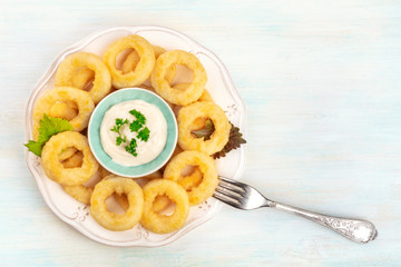 A plate of squid rings, shot from the top with a fork, mayonnaise sauce, and a place for text