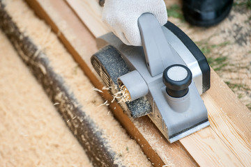 The hand of a man working with electric planers outdoor. Shavings debris ejected from the machine....