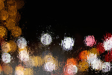Bokeh night city lights behind wet glass during rain. Can be used as wallpaper or background