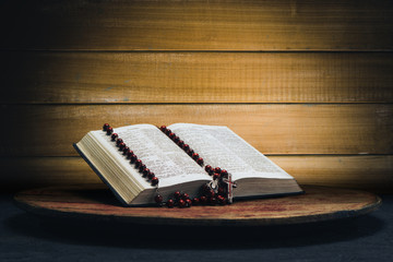 Bible and the crucifix beads on a old round table. Beautiful yellow wooden background. Religion concept.