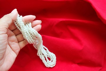Close up of pearl necklace on woman hand and red background. 