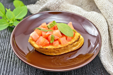 Bruschetta with tomato and basil in brown plate on dark board