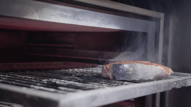 Hand in black gloves putting fish salmon inside the oven with charcoals for grilling