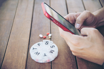 People using mobile phone to prepare daily medicine tablet in pillbox - people healthcare with...