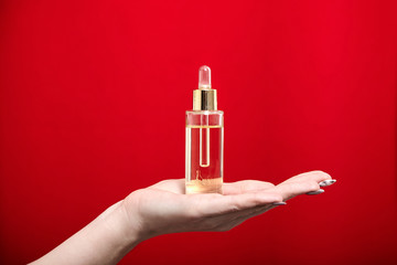 Pipette bottle with cosmetic oil  in female hand on red background. Skin care product