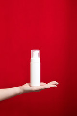 Female hand with a blank white cosmetic bottle on red background