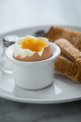Gekochtes Ei im Eierbecher mit Eierlöffel, Salzstreuer und Toast Brot beim Frühstück