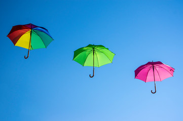Group of flying umbrellas isolated on blue background, ready for the rain, wallpaper background, bright various colors