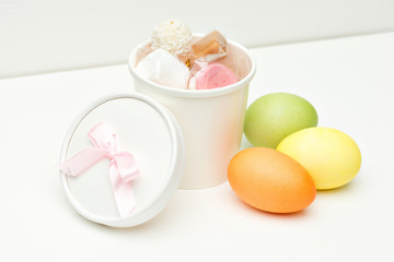 Colored easter eegs with cup of candies on white wooden background