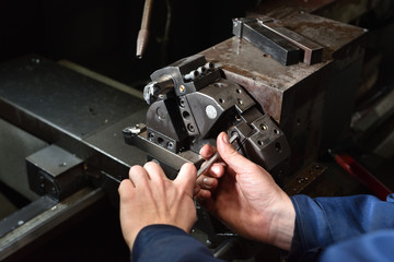 A worker in blue workwear performs maintenance on the CNC machine to install drills in the turret for working with metal. Hands of the worker close up, screw various drills