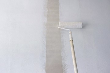 Long handle roller brush applying primer white paint on cement wall background