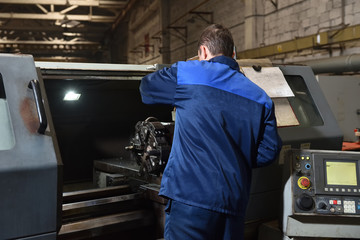 A worker in blue work wear, performs maintenance on the machine CNC to install new drills for working with metal. Back view