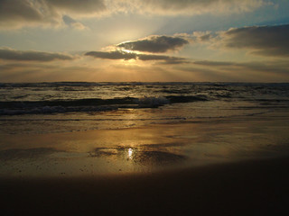 Obraz premium Sunset view on a calm sandy beach with cloudy sky and golden light.
