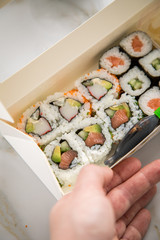 Frau isst Maki und Inside Out California Sushi vom Lieferdienst mit Lachs, Surimi, Avocado, Gurken mit Ingwer, Wasabi und Soja Soße in Einweg Bento Box Verpackung