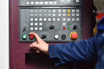 Worker in blue workwear holds hands on the control panel of the CNC machine. Close-up