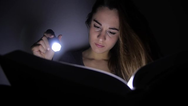 portrait of a girl close up she sits with a flashlight and turns the pages of a book in a dark room