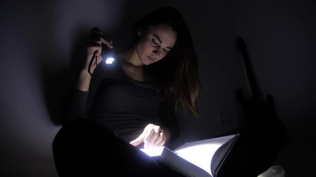 close-up portrait girl is reading a book with a flashlight in a dark room at night. 4k. Motion shooting