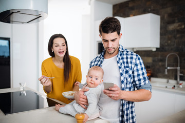 A young family at home, a man holding a baby and a woman feeding her.