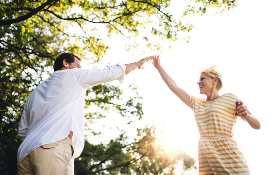 A Young Couple Spending Time Together In Nature In Summer, Making High Five.