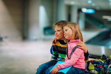 little boy and girl wait in airport, sit on luggage,