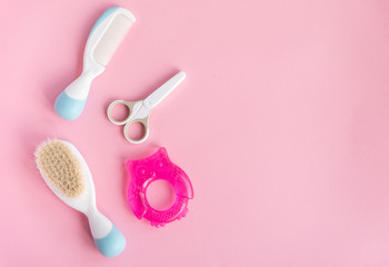 Little opened scissor, brushes and toys for baby care. Close up of metal and plastic scissors for child care. Pink studio background. Concept of cutting baby nails.