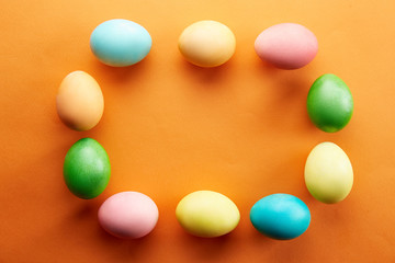 Bunch of blank painted Easter eggs of different pastel color on bright orange paper background with a lot of copy space for text. Top view, flat lay, close up. Easter greeting card concept.