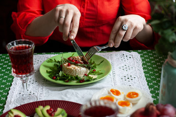 A woman in a red blouse cuts a baked camemberle, in the frame only hands. Healthy nutritious lunch or dinner for two