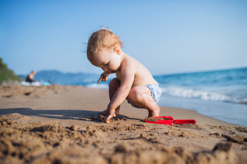 A small toddler girl sitting on beach on summer holiday, playing.
