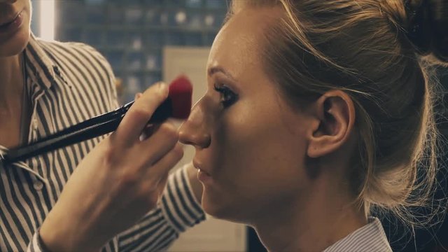 Professional makeup artist putting cosmetics on blonde model face