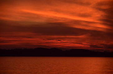 Telephoto into the deep red after-sunset sky, with aocean and a remote silhouette landscape.