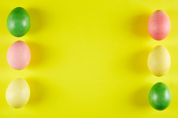 Bunch of blank painted Easter eggs of different pastel color on bright yellow paper background with a lot of copy space for text. Top view, flat lay, close up.