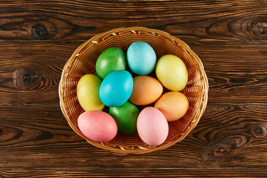 Beautiful easter table composition. Pile of painted eggs of different passtel colors in wicker basket on textured table background. Greeting card template. Copy space, close up.