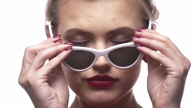 A woman with red lipstick is putting on her white stylish sunglasses, close up