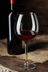 Bottle and glass of red wine on wooden barrel shot with dark wooden background