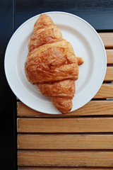 Big pasrty croissant on a white plate on wooden table