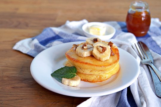 Cornmeal pancakes on a white plate. Served with bananas, walnuts and honey or maple syrup.