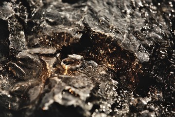 Beautiful wedding rings lie on the stones, on which the water flows. Declaration of love, spring. Wedding Card, Valentine's Day greetings. Wedding rings Details of the wedding day