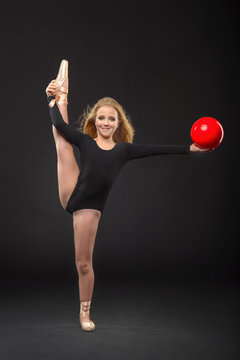 Cute little ballerina with long hair in a black leotard and pointe posing on a black background