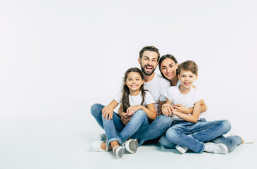 Relationship concept. Beautiful and happy smiling young family in white T-shirts are hugging and...