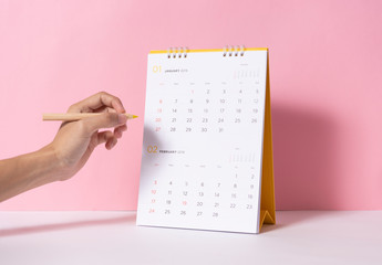 Hand holding pencil for writing marking on paper spiral calendar year 2019 on pink background.