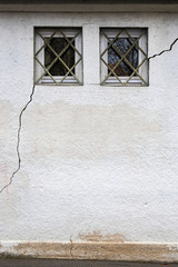 Fassade mit 2 kleinen, vergitterten Fenstern durch die ein langer und breiter Riss von ca. 3 Meter im Mauerwerk verläuft