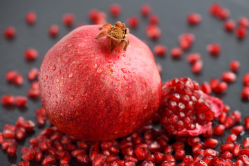 Ripe pomegranate and seeds scattered on black stone background