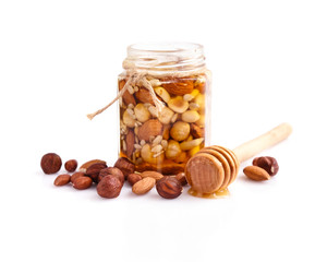 A honey jar with a spoon for honey and different nuts on white background